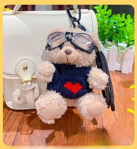 Detail of plush bear keychain with goggles and blue sweater on white leather bag