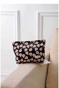 Detailed texture of black floral corduroy makeup bag placed on a cozy beige sofa armrest