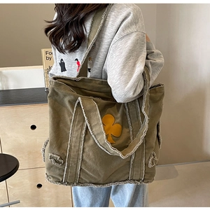 Detail of army green canvas tote bag featuring raw edges and a yellow club pattern patch