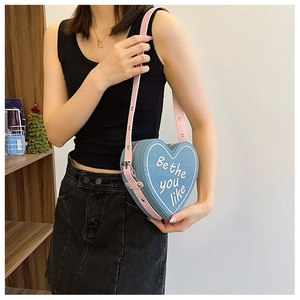 Détail d'un sac à bandoulière en denim bleu en forme de cœur avec lanière en cuir rose