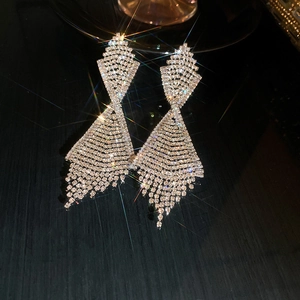 Close-up of sparkling rhinestone tassel long drop earrings on a dark reflective surface