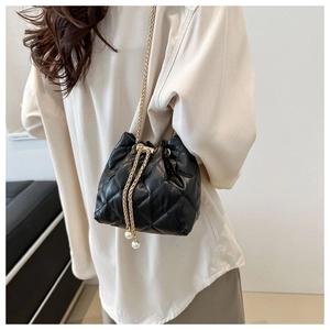 Detail of black quilted bucket bag with gold chain strap and pearl drawstring accents