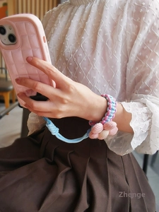 Detailed view of pink and blue woven phone wrist strap with soft plush flower charm