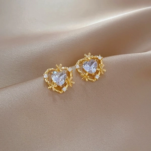 Macro shot of gold heart-shaped stud earrings with zircons on beige silk fabric