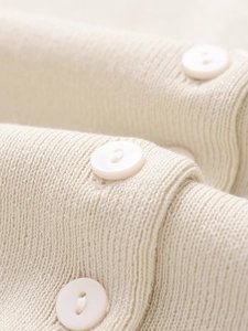 Detailed macro view of the cream knit fabric and smooth round buttons on the cardigan