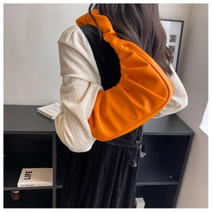 Close-up of bright orange pleated leather shoulder bag with wide strap detail