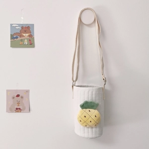Detailed close-up of a quilted beige bottle bag with a plush pineapple embroidery detail