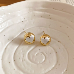 Detailed view of golden heart earrings with silver accents on a white ceramic tray