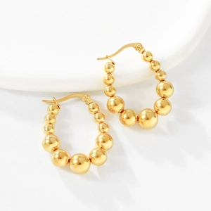 Close-up of golden beaded hoop earrings with polished spheres and secure clasp