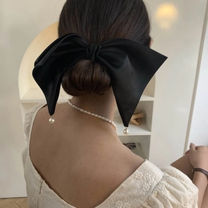 Detail of elegant black satin bow hair clip with pearl pendants worn on hair bun