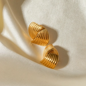 Macro detail of golden spiral shell textured earrings resting on elegant beige silk fabric