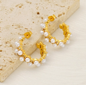 Detailed close-up of gold C-shaped earrings with pearls and zircons on travertine