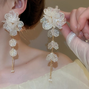 Detailed view of white acrylic flower earrings with golden tassels on a model
