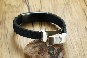 Close-up of black silicone ID bracelet with brushed steel plate on a natural stone surface
