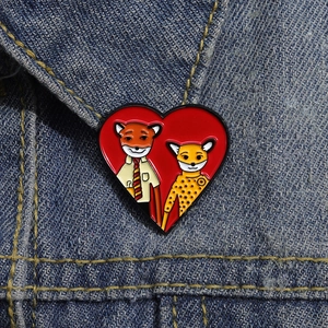 Close-up of a heart-shaped enamel pin featuring cartoon animals on a denim jacket