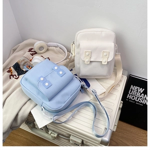 Light blue and beige canvas crossbody bags displayed with a white suitcase and hoodie