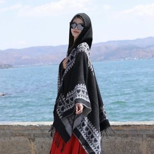 Détail d'un poncho en tricot noir à capuche avec motifs de cœurs et ourlet à franges