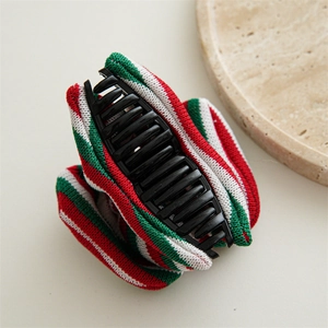 Detail view of a red, green, and white striped knit fabric hair clip on a beige surface