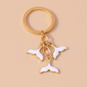 Détail d'un porte-clés doré avec trois pendentifs queue de poisson en émail blanc