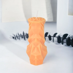 Oranje geometrische geurkaars in ruitvorm met modern gefacetteerd ontwerp op wit bureau