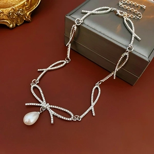 Silver bow necklace with sparkling rhinestones and teardrop pearl pendant on tray