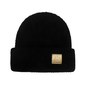 Close-up of black ribbed knit beanie featuring a gold square smiley face logo patch