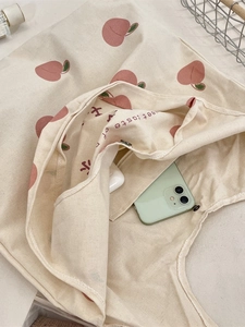 Canvas tote bag with pink peach prints and internal pocket holding phone and earbuds