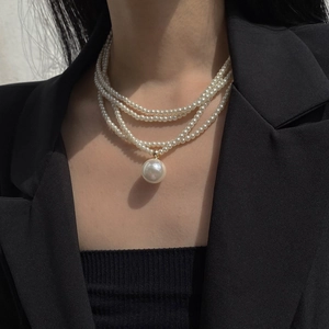 Detail of three-layer pearl necklace with a large round pendant on a black blazer