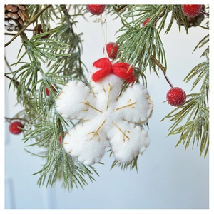Detailed view of white felt snowflake ornament with red bow on a festive pine branch