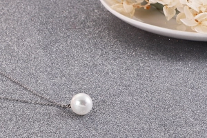 Vue détaillée d'un collier en acier titane argenté avec un pendentif perle ronde blanche