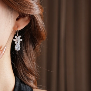 Close-up of a silver flower drop earring with a teardrop zircon on a female model