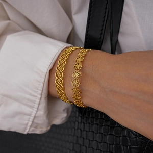Detail of golden hollow-out bangle and daisy flower bracelet worn on wrist