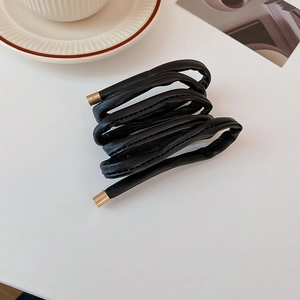 Macro detail of black leather hair wrap with gold metal tips on a clean minimalist desk