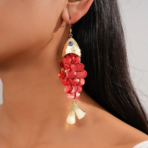 Macro detail of large gold fish-shaped earring with red sequins and blue eye