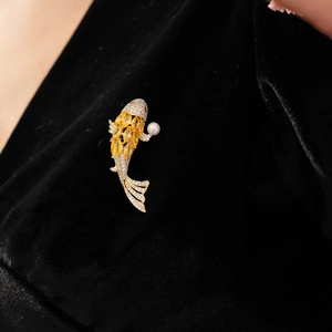 Detailed close-up of a gold carp brooch with sparkling crystals and a white pearl accent