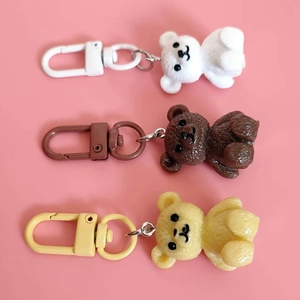 Three colorful resin cartoon bear keychains in white, brown and cream on pink background