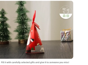 Pyramid-shaped red Christmas gift box with Santa motif and ribbon on wood surface