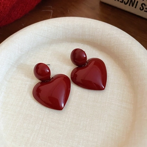 Close-up of heart-shaped dark red resin drop earrings with round ball studs on tray