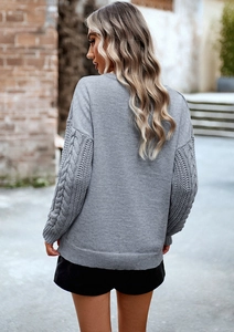 Dettaglio del retro di un maglione grigio in maglia con motivi a treccia sulle maniche