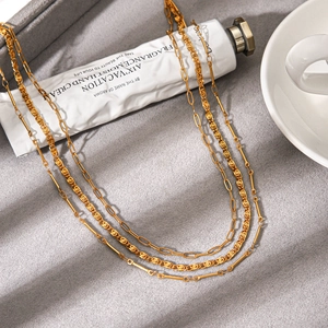 Three-layer gold titanium steel stacked necklace displayed on a luxury grey fabric background