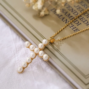 Minimalist gold-plated cross pendant necklace with pearls on a vintage background
