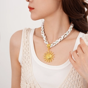Detail of bohemian sun pendant necklace with white woven rope and gold metal accents