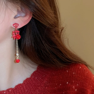 Macro detail of asymmetric red tassel earrings with Rich text and Fu character charm