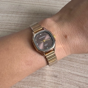 Close-up of a women's square gold watch with a deep brown dial worn on a wrist