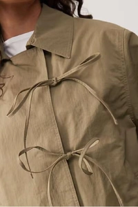 Detailed view of khaki windbreaker featuring decorative front tie-up bows and lapel collar