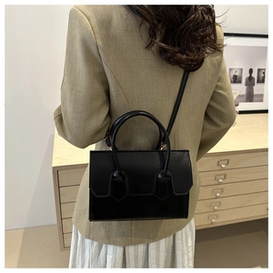 Modern black leather handbag worn by a model in a minimalist interior setting