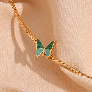 Close-up of a 18K gold-plated butterfly pendant with green and blue enamel on a flat chain