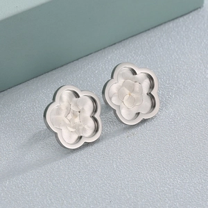 Brushed stainless steel flower shaped stud earrings on a textured grey background