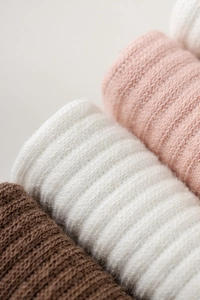 Macro detail of three pairs of rolled knitted five-toe yoga socks in brown, white and pink