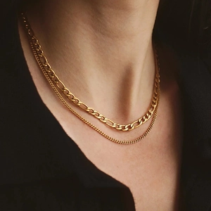 Detail of layered gold Figaro and Curb chain necklaces on model showing metal texture